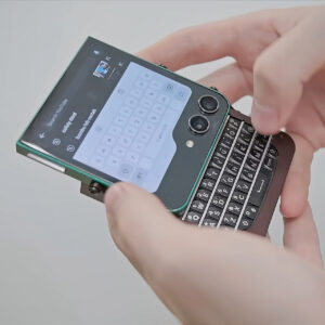 Close-up of hands holding a small device with a physical keyboard, typing